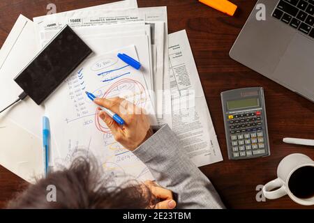 A business woman wearing formal dress is working at an office setting. She is calculating income and expenses using statements, pay slips, receipts. S Stock Photo