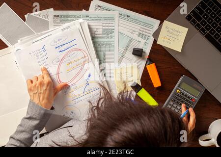 A woman is preparing her tax return in her office using forms calculator laptop and various notes as well as bills. Tax return in USA involves a thoro Stock Photo