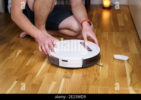 Housework and technology concept. Maintenance and service of robot vacuum cleaner. Cleaning, repair, replacement of parts. Man repairing robot cleaner Stock Photo