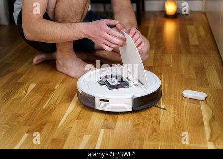 Robot vacuum cleaner repair. Man fixing robot vacuum cleaner DIY at home on the floor. Robotic vacuum cleaner maintenance and service. Smart device fo Stock Photo