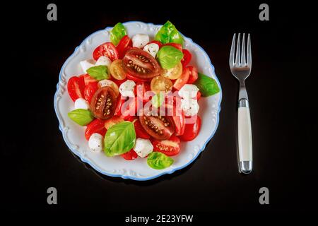 Cherry tomato with mozzarella cheese on white plate with fork. Close up. Stock Photo