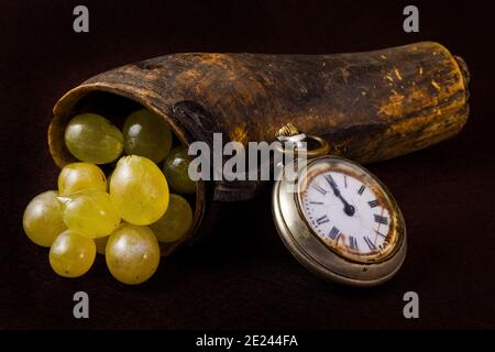 Pieces of grapes in an old horn and an antique clock on a black background Stock Photo