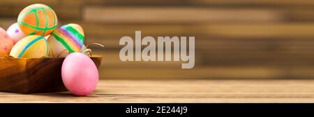 colorful easter eggs in a wooden plate on a wooden background, banner. Stock Photo
