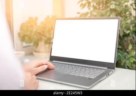 hand typing mockup laptop computer showing blank white screen on table office place. blank screen laptop computer template. Notebook screen for applic Stock Photo
