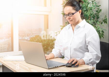 middle-aged business woman using laptop notebook on wooden desk at home office workspace. Distance learning online education and work. Stock Photo