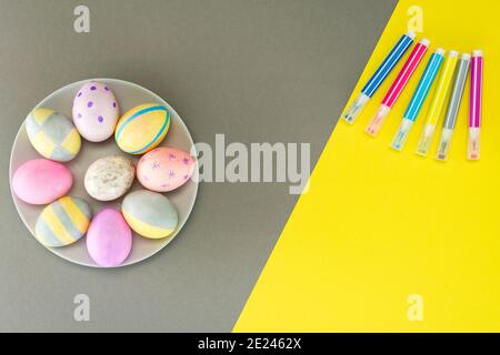 Colorful Easter eggs in a gray plate on a yellow-gray background and felt-tip pens for decor with place for text. View from above. Pantone trend 2021. Stock Photo