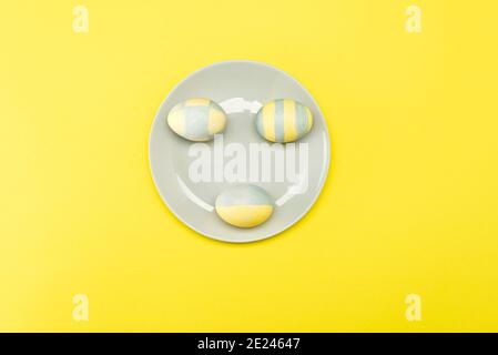 Easter eggs painted yellow-gray in a gray plate on a yellow background. Pantone Trend 2021. Stock Photo