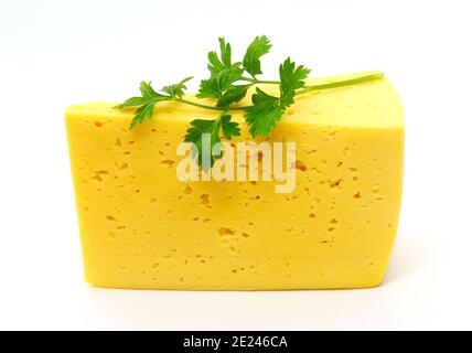 An isolated Russian cheese slab, semi hard cheese with small eyes, holes with a branch of parsley on top on a white background. Stock Photo