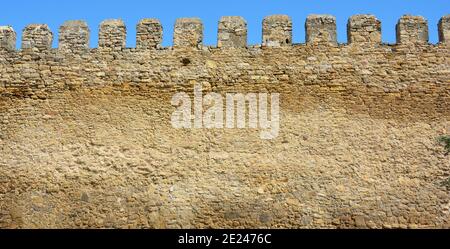 A part of an ancient fortress wall, castle wall with a tooth shaped parapet made from limestone bricks, coquina rocks, yellow shell rocks against the Stock Photo