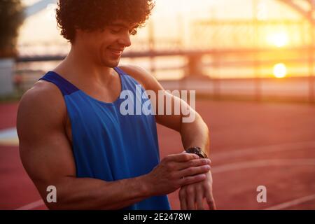 Young smiling fit man checking his watch before the training starts. Early summer morning work out. Stock Photo