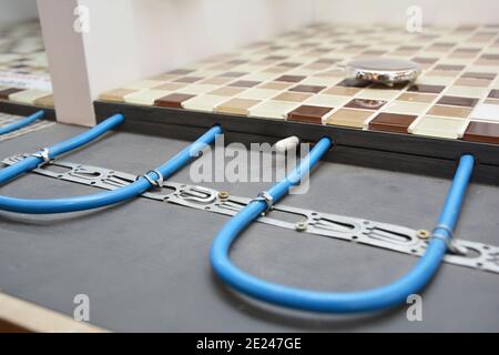 Installing a radiant floor heating system with a close up of heating cables fastened to the floor underlayment under ceramic mosaic bathroom floor whi Stock Photo