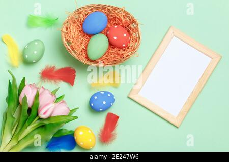 Happy easter. Multicolored eggs in a basket, flowers and frame with copy space on a mint green background. Stock Photo