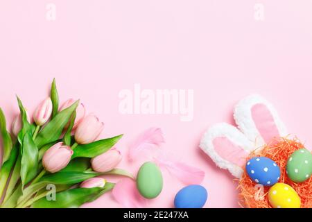 Happy easter. Multi-colored eggs in the nest, rabbit ears, flowers on a pink background. Flat lay greeting card. Stock Photo