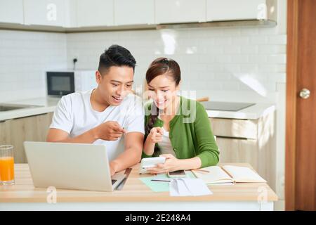 Photo of cheerful loving young couple using laptop and analyzing their finances with documents. Look at papers. Stock Photo