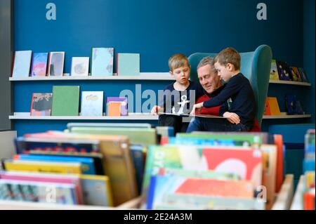 Grandfather reading book to grandsons in library Stock Photo