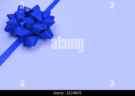 Decorative blue ribbon bow on blue background with copy space for text. Giving presents concept. Greeting card or holidays sale background. Selective Stock Photo