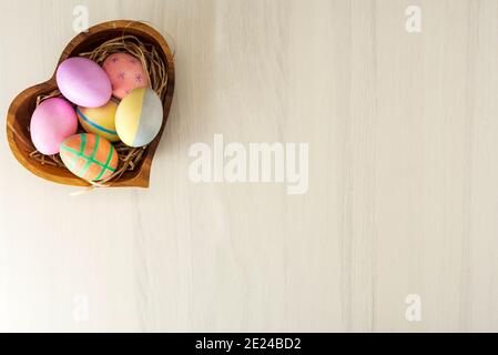 Colorful easter eggs in wooden plate on gray table with place for text, top view. Stock Photo