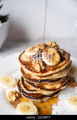 Maple syrup pouring onto a delicious homemade banana pancake stack with nuts Stock Photo