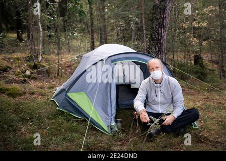 Man wearing face mask sitting in front of tent Stock Photo
