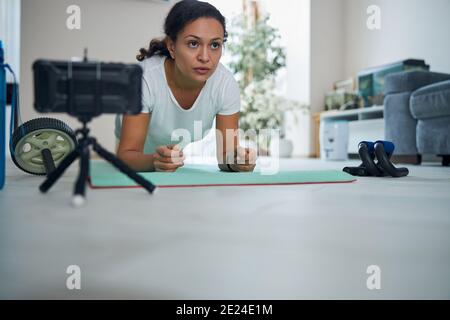 Serious dark-haired vlogger performing the core-strengthening exercise Stock Photo