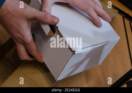 Delivery and checking online shopping concept. Man holds parcel in white rectangular cardboard box. Side view at an angle. Selective focus. Stock Photo