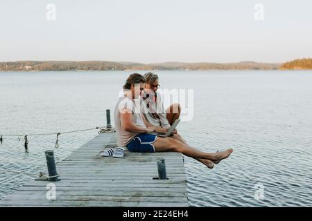 Mother with adult son on jetty looking at laptop Stock Photo