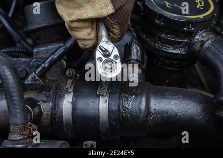 Car repair, car service concept. Gloved hand with wrench tightens  bolts in the engine compartment of  truck.  Selective Focus. Stock Photo