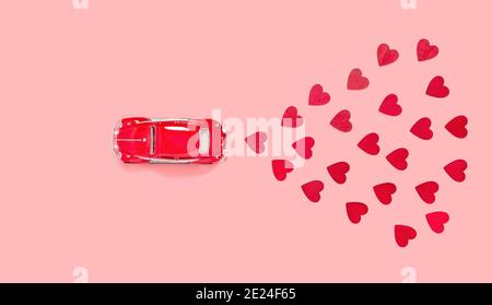 Fulda, Germany - DEC 18, 2020: Red retro toy car with many red hearts for Valentines day on pink background from above. Love and holiday theme, top vi Stock Photo