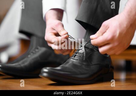 Businessman tying shoelaces on classic elegant black leather shoes, or groom dressing in preparation for wedding day. Close-up shot from the side Stock Photo