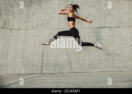 Sporty woman doing running and jumping exercise outdoors. Fitness female athlete exercising outdoors. Stock Photo