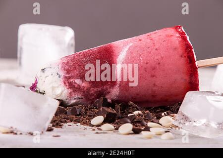 Strawberry ice cream popsicle lolly pops with whipped cream decorated chocolate and ice cubes on white wooden background. Close up Stock Photo