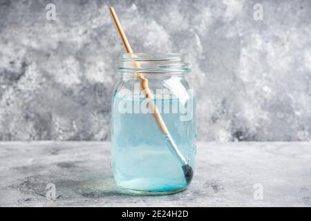 Artistic brushes in a jar with water on the gray rustic background. Artist tools. Selective focus. Stock Photo