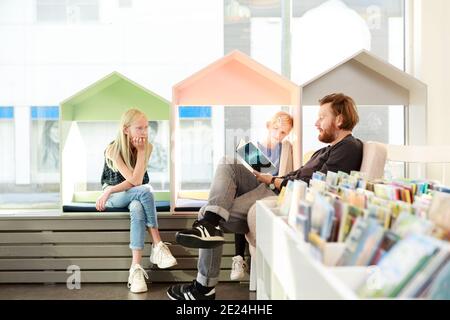 Father reading daughters book in library Stock Photo