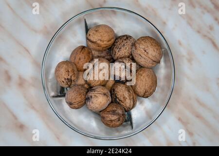 White bowl with black edges on the table, filled with some walnuts Stock Photo