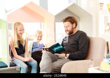 Father reading daughters book in library Stock Photo
