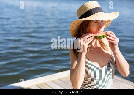 Woman on jetty eating watermelon Stock Photo