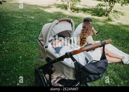 Baby boy sleeping in pram, parents in background Stock Photo