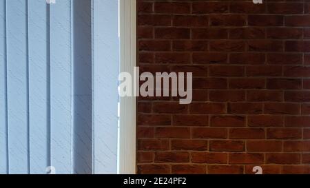 Large window with vertical white or gray blinds, loft, brick wall, industrial interior. Sunlight from a window on brick walls in a room or office Stock Photo