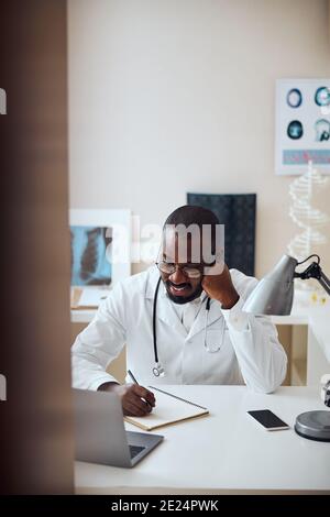 Joyful physician propping the cheek during filling of notepad Stock Photo