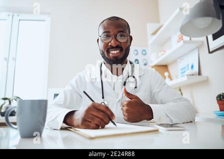 Multiethnic medical person with a pencil giving thumbs-up Stock Photo