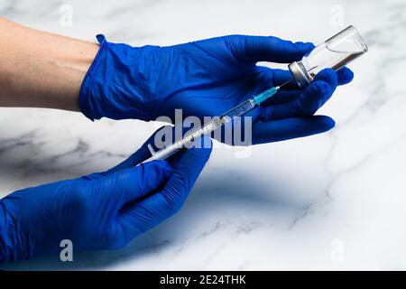 Hands in surgical gloves preparing Medical syringe and needle for hypodermic injection on a marble counter top. Stock Photo