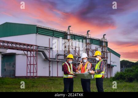 Three engineers looking at construction plans in front of a factory, Thailand Stock Photo