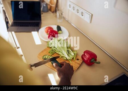 Adult man chopping a cucumber on a kitchen board Stock Photo
