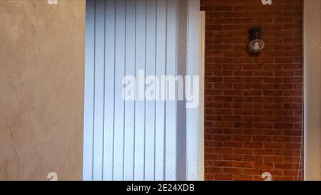 Large window with vertical white or gray blinds, loft, brick wall, industrial interior. Sunlight from a window on brick walls in a room or office Stock Photo