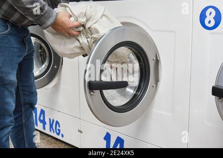 Cropped Hands Of Man Putting Clothes In Washing Machine At laundry service Stock Photo