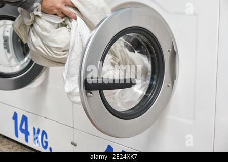 Cropped Hands Of Man Putting Clothes In Washing Machine At laundry service Stock Photo