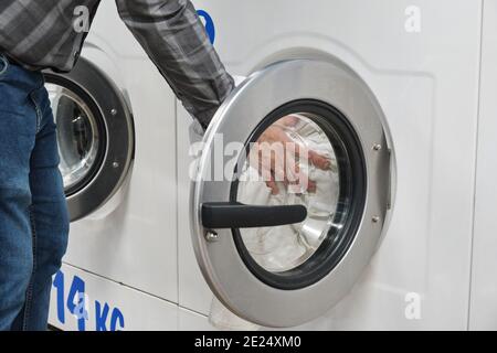 Cropped Hands Of Man Putting Clothes In Washing Machine At laundry service Stock Photo