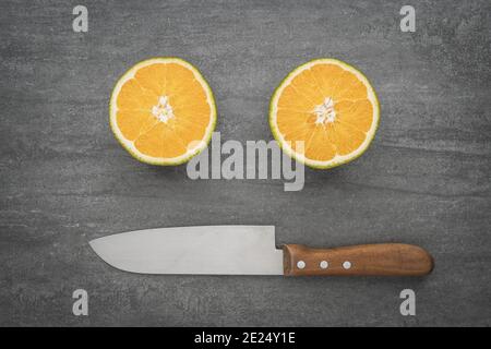 A smiley face made of a knife and oranges. Healthy citrus fruit full of vitamins cut in half. Stock Photo