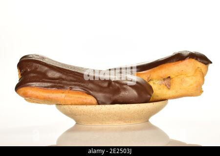 Two chocolate eclairs on a ceramic saucer, close-up, isolated on white. Stock Photo