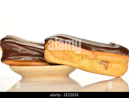 Two chocolate eclairs on a ceramic saucer, close-up, isolated on white. Stock Photo
